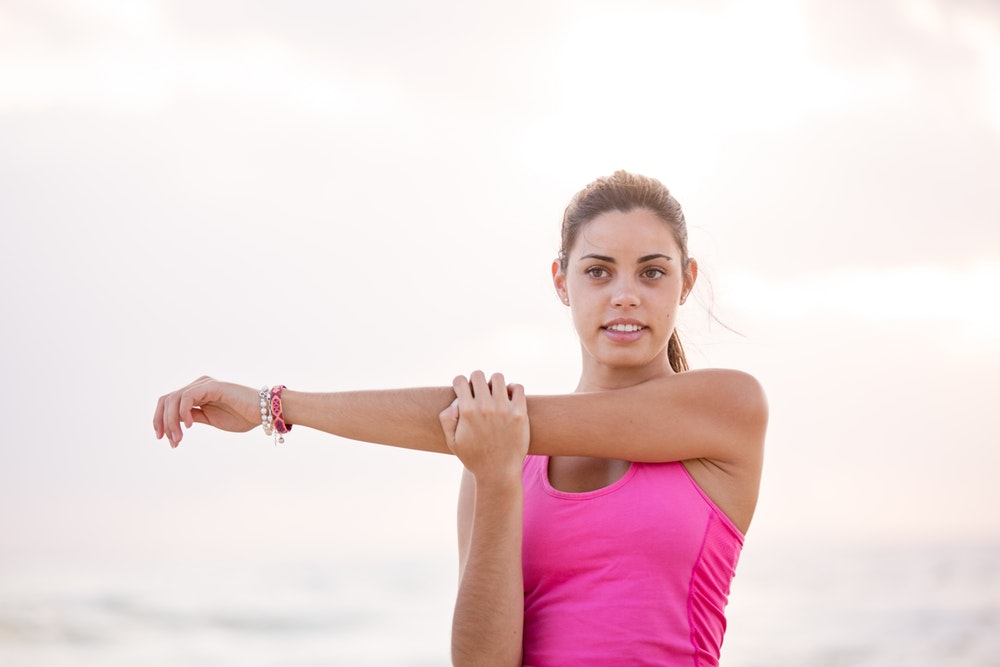 Pretty girl in pink tank top streches her shoulder