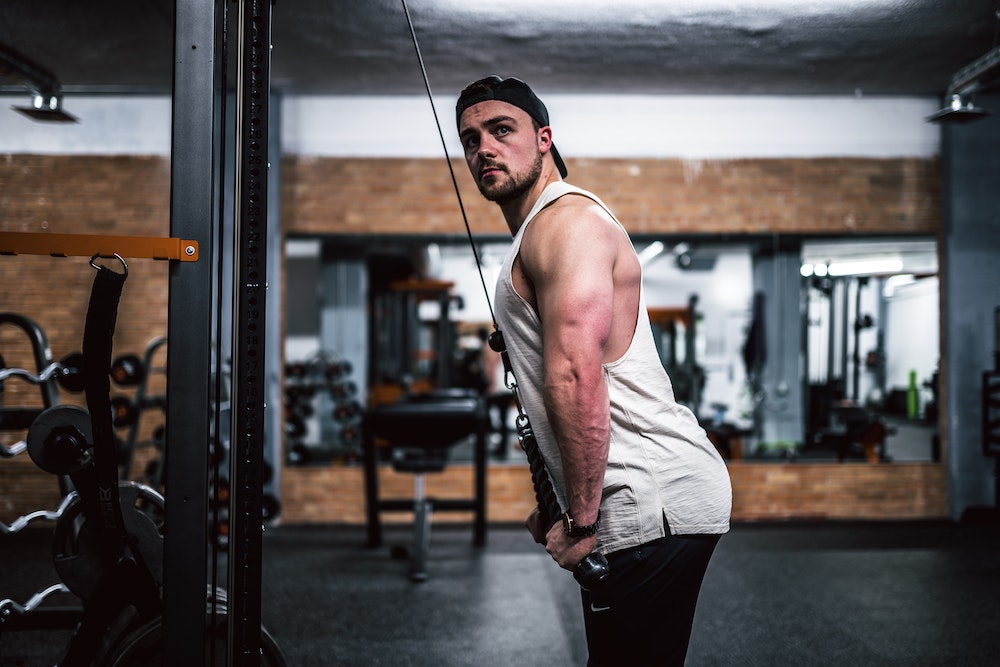 Man in white tank top and black hat doing a lat pulldown